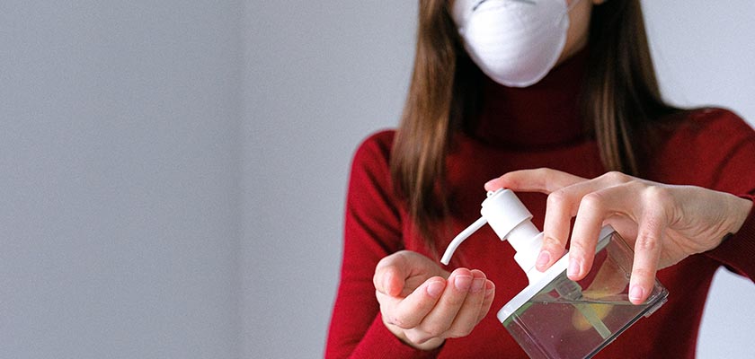 woman wearing a mask applying hand sanitizer
